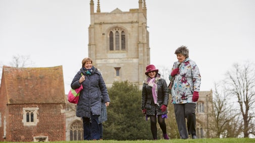 Three visitors dressed in winter wear with a church and outbuilding in the background